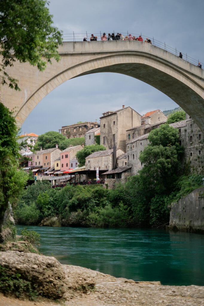 A dramatic side-profile view of the Stari Most (Old Bridge) in Mostar, reflecting in the turquoise Neretva River during the golden hour.