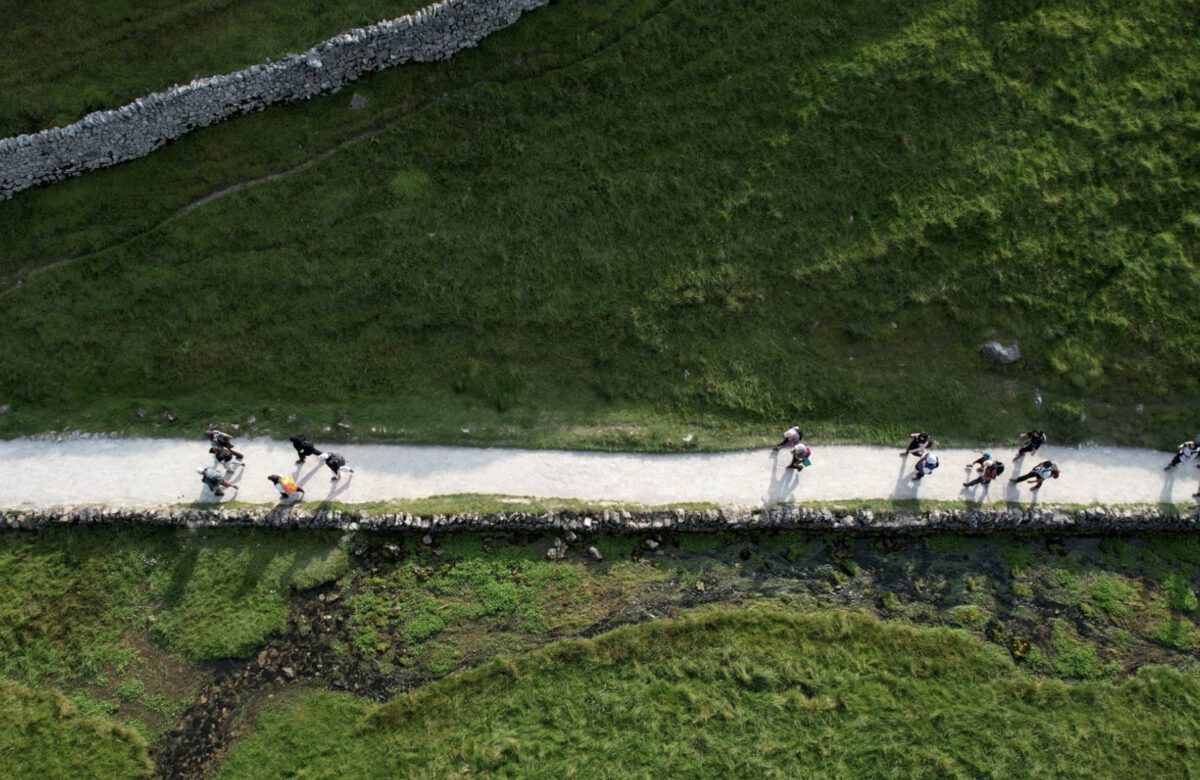 drone photo of muslim hikers in english countrside, beautiful, sunny day, green mountains, stone walls, white paths.