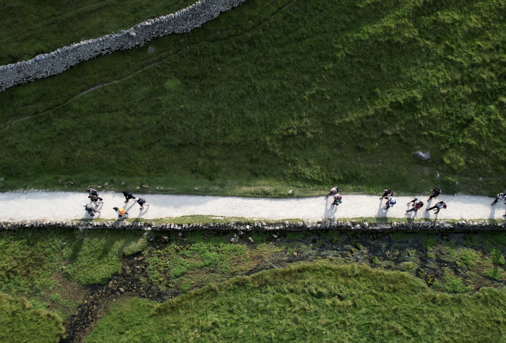 drone photo of muslim hikers in english countrside, beautiful, sunny day, green mountains, stone walls, white paths.