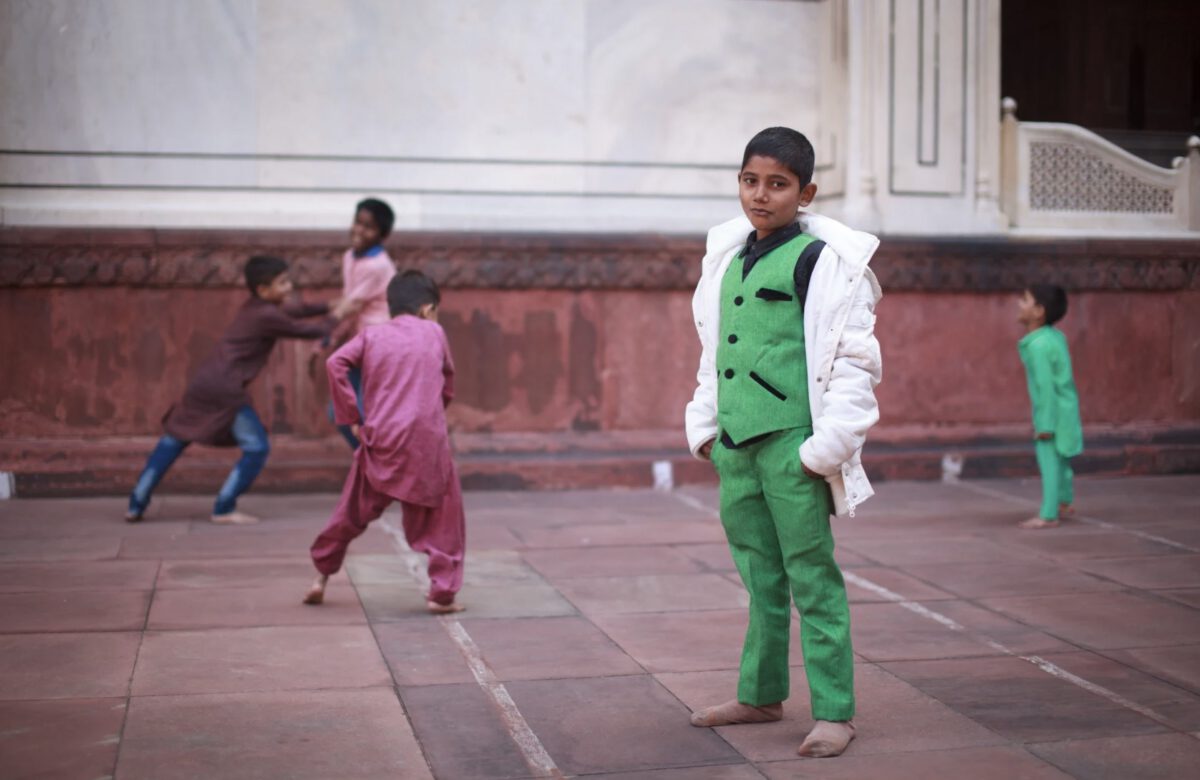 An Indian kid posing for the camera in the Moti Masjid (Pearl mosque) in Delhi, India, while other kids play in the background.