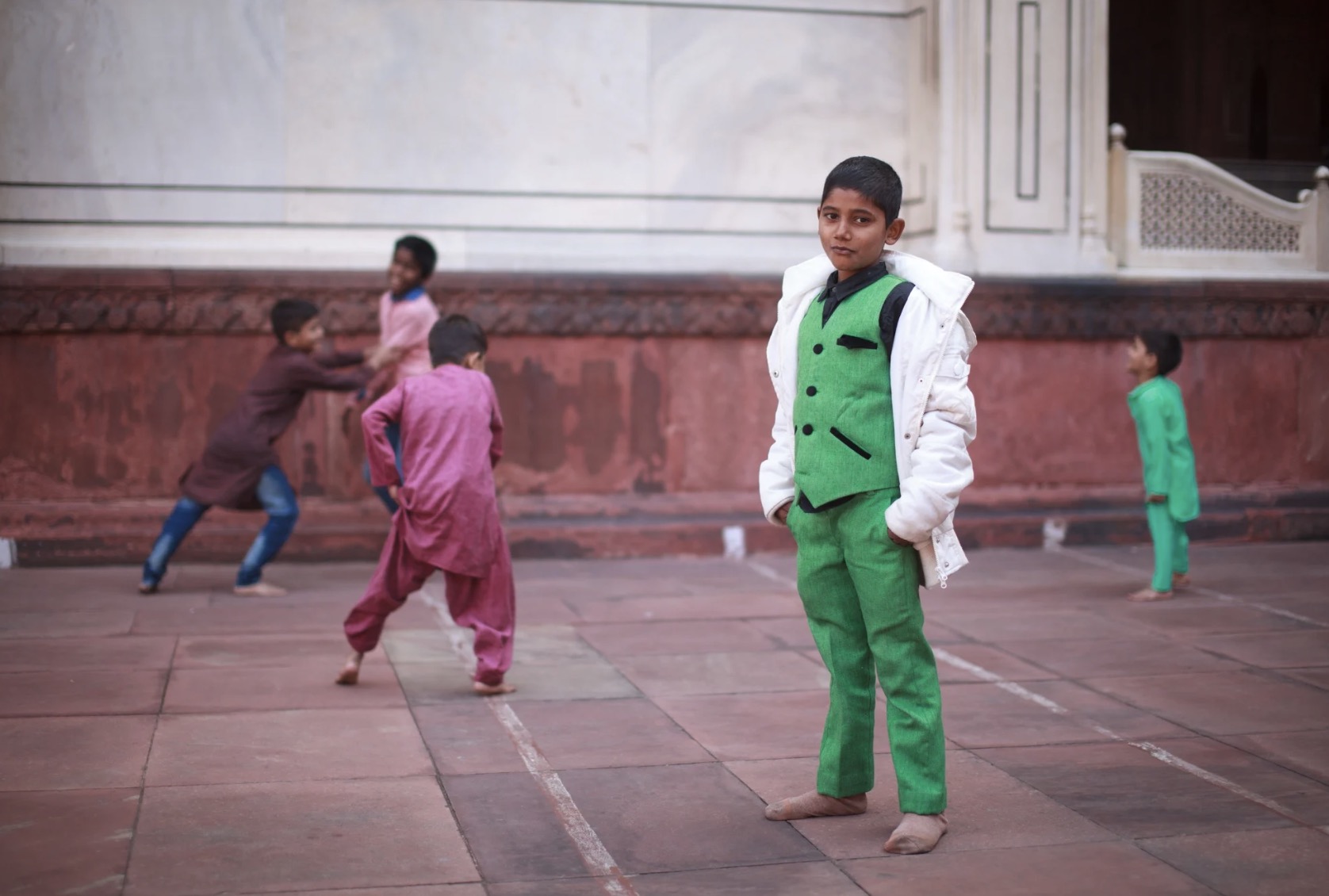 An Indian kid posing for the camera in the Moti Masjid (Pearl mosque) in Delhi, India, while other kids play in the background.